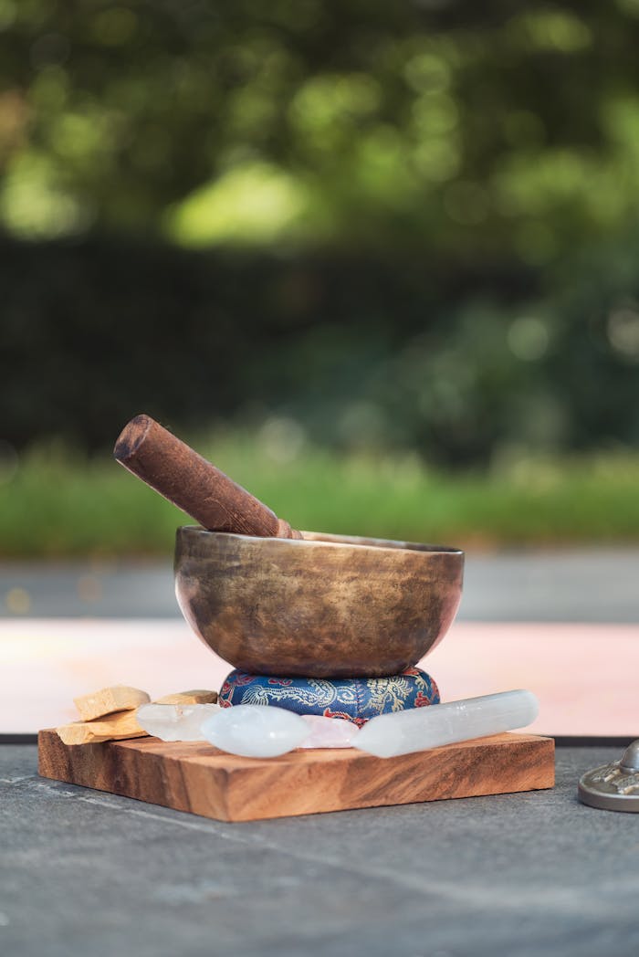 A bronze singing bowl on a patterned cushion with healing crystals and wooden base, perfect for meditation.